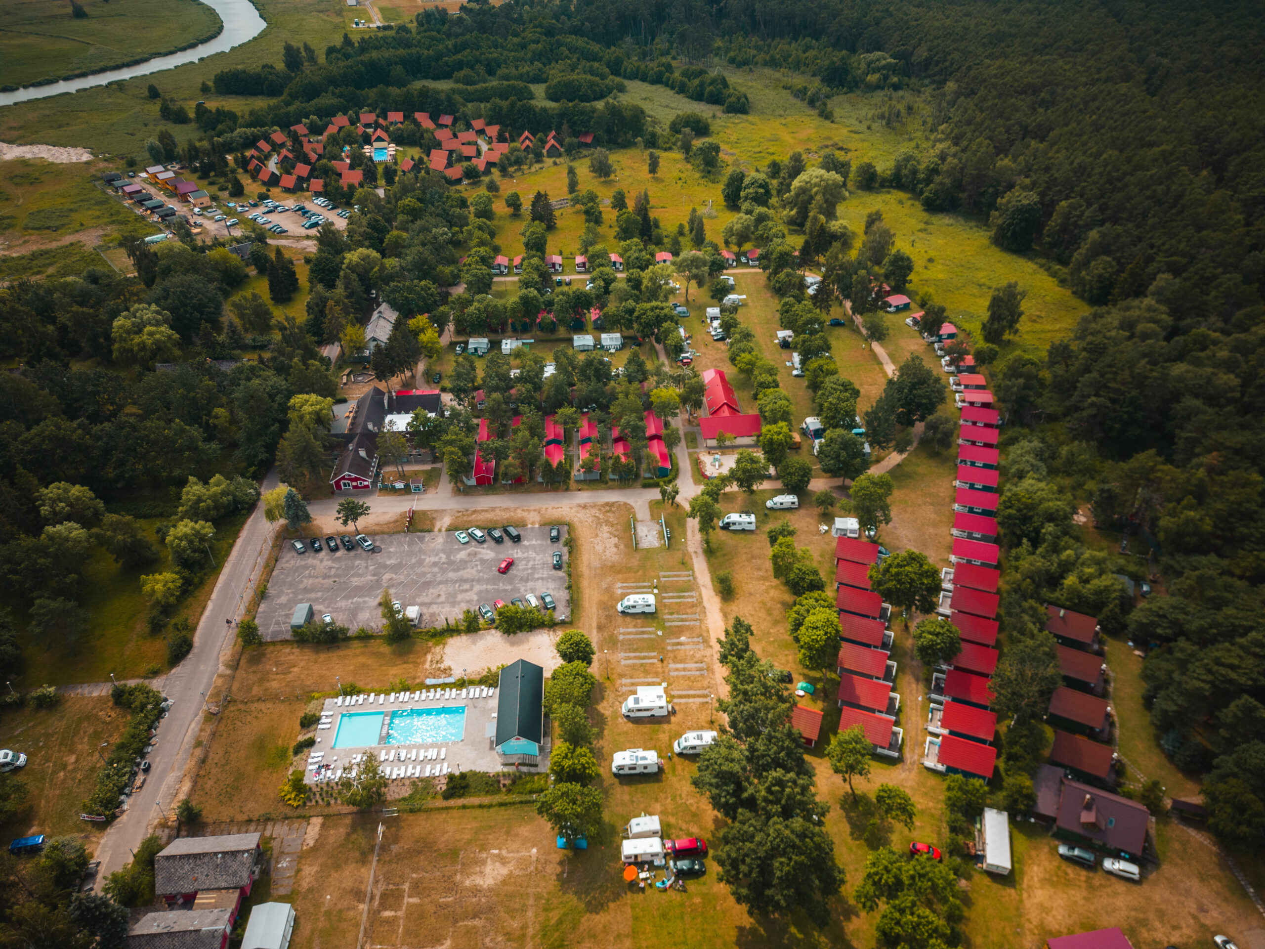Widok z góry na InterCamp’84 Łeba – duże pole campingowe z domkami, kamperami i basenem, położone w otoczeniu lasów i natury.