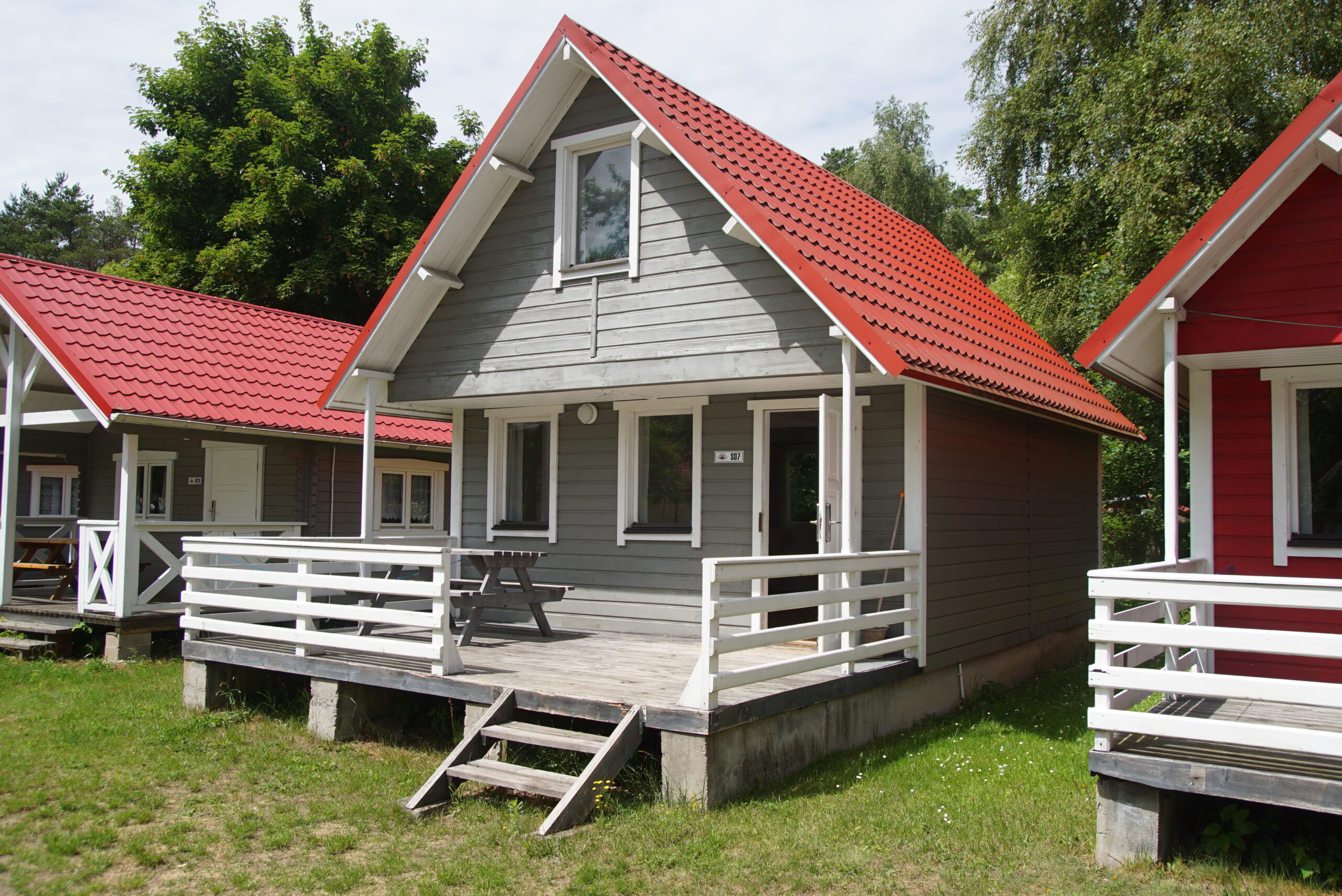 Domki letniskowe na campingu InterCamp’84 Łeba – zadbane obiekty wakacyjne w otoczeniu drzew i alejek spacerowych.